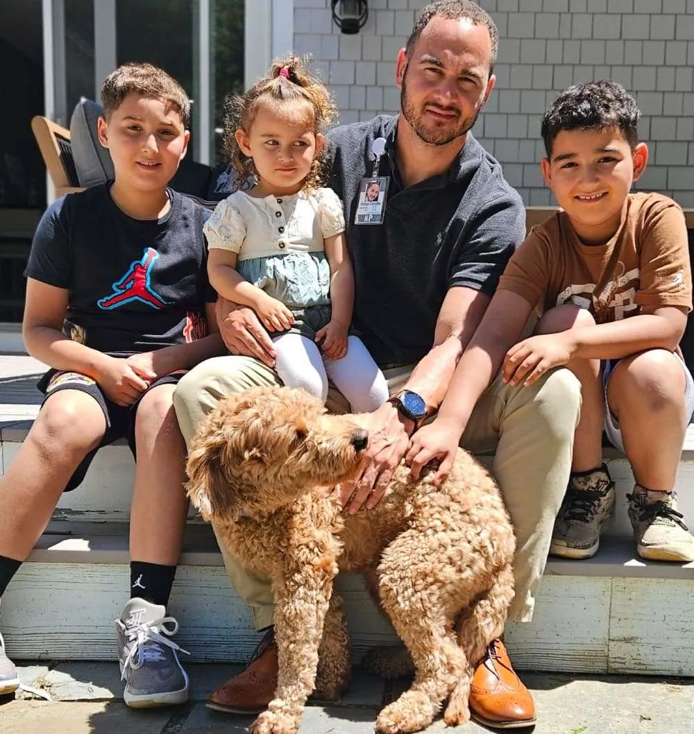 The family behind Mini Goldendoodles of Cape Cod on porch steps petting their apricot Goldendoodle